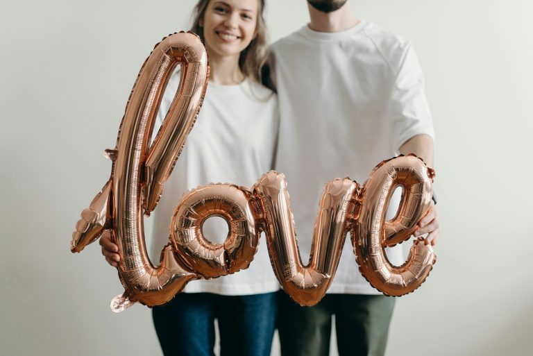 A couple in white t-shirts holds a metallic love balloon, symbolizing affection and joy.